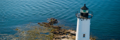 Portsmouth Harbor Lighthouse with clear, blue water ripples and rocky seaweed in the background