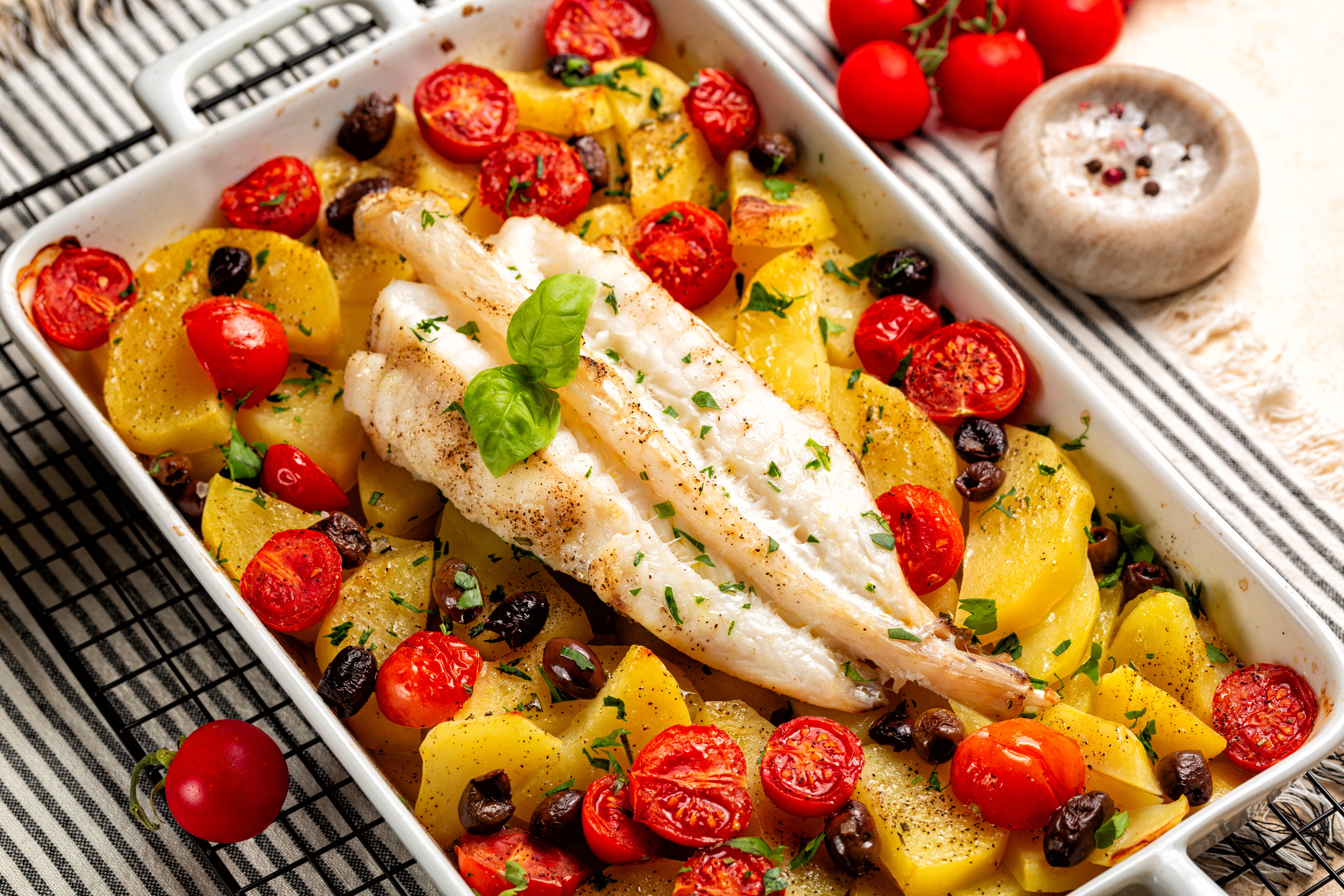 Seafood on a baking pan with tomatoes and potatoes.