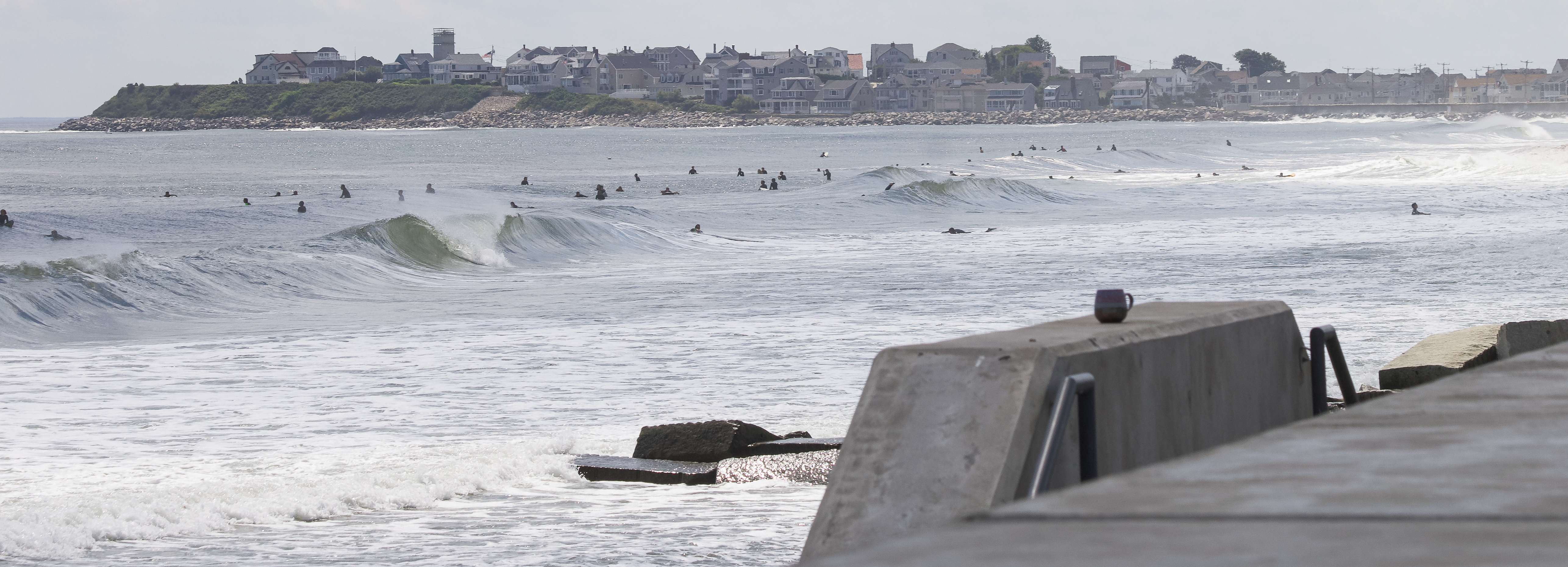 The beach wall in Hampton, NH in the foreground with surfers in the background. 