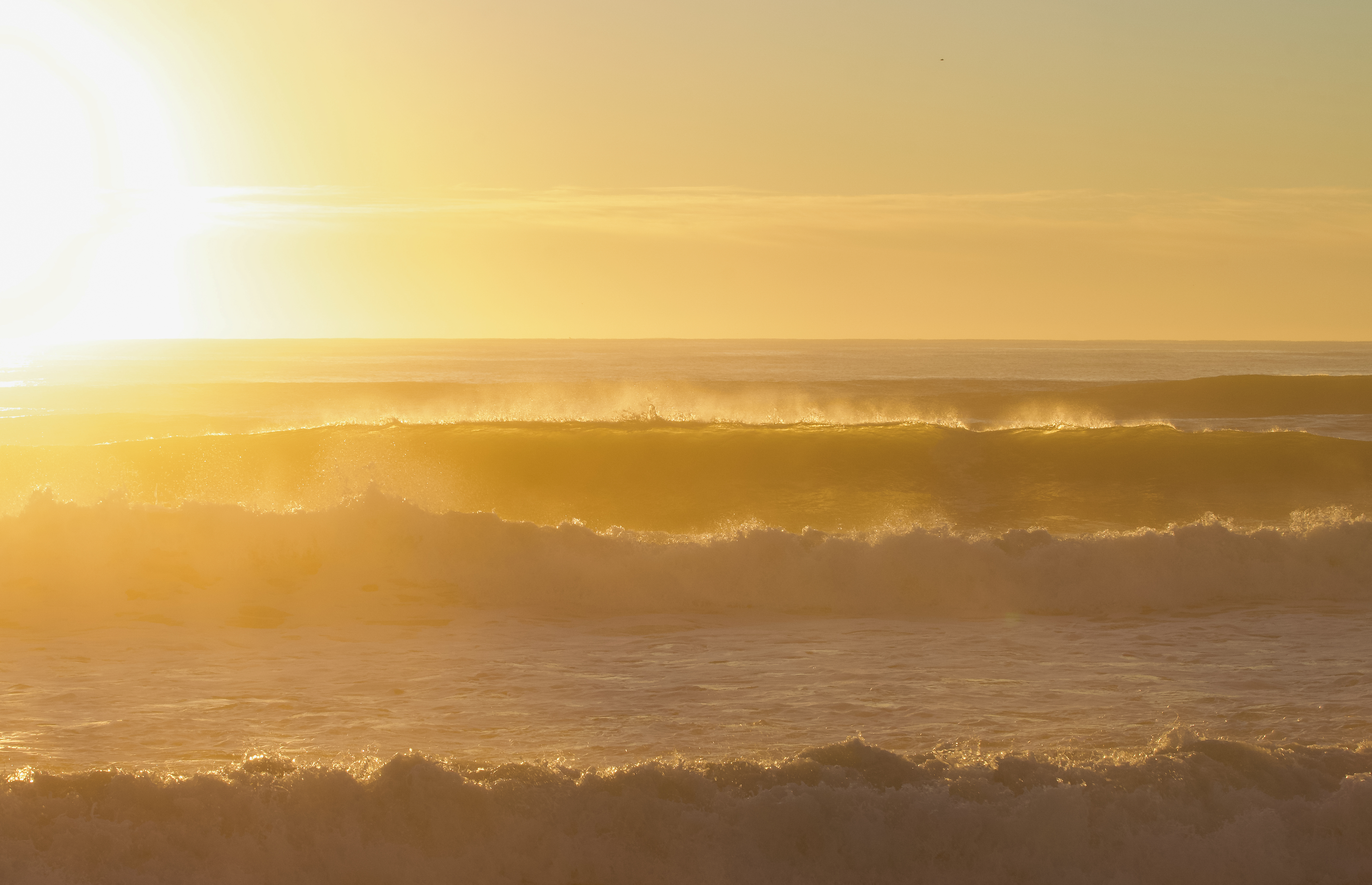 Sunrise looking out at the coast with large, breaking waves and a yellow sky.