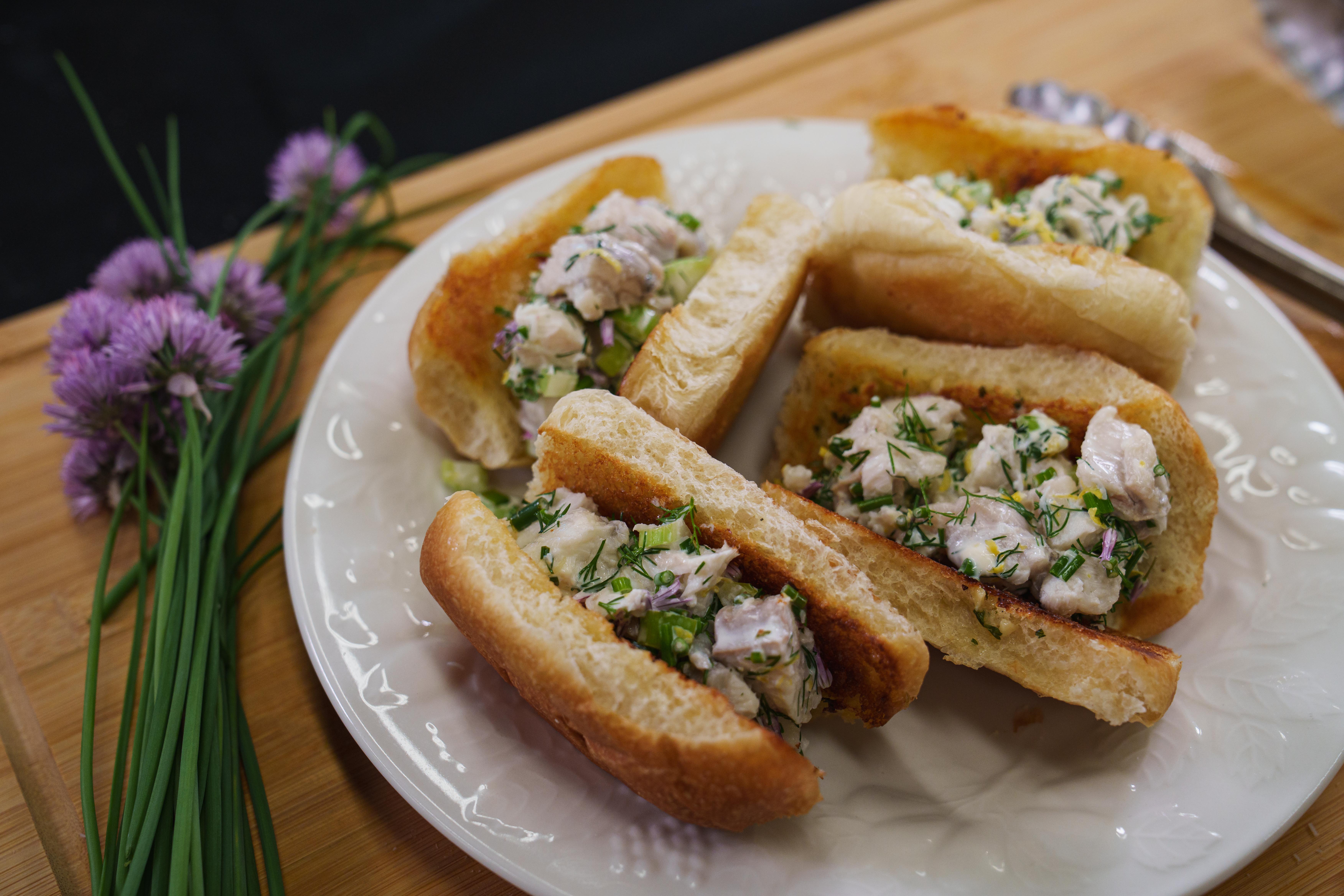 Monkfish rolls on a plate with chive blossoms next to them. 