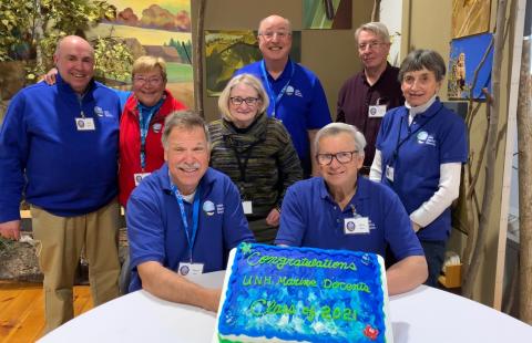 8 volunteers from the UNH Marine Docent Class of 2021-2022 stands behind their graduation cake
