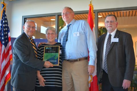 Man and woman receive award plaque from two men in suits.