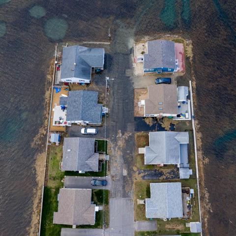 An aerial view of flood water surrounding and flooding a road extending into a marsh, isolating homes