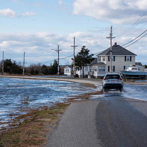 A car drives through floodwaters encroaching a road