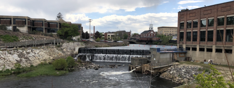 A dam on a river between buildings, with a fishway spilling into the water in the foreground, Jackson Mills Dam in Nashua, NH on the Nashua River