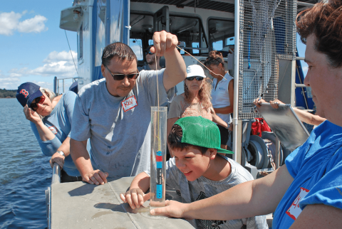 a young boy and an adult male collect a water sample aboard a research vessel