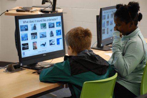 two young students review a virtual marine science activity on a computer screen in a computer lab