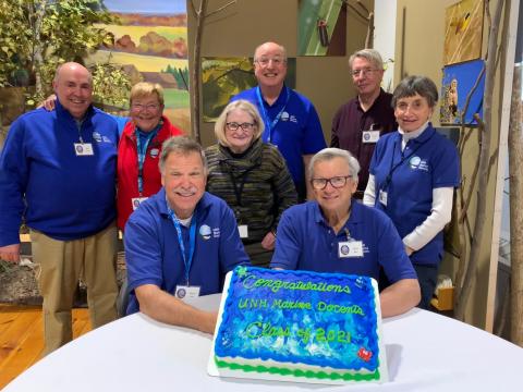 8 volunteers from the UNH Marine Docent Class of 2021-2022 stands behind their graduation cake