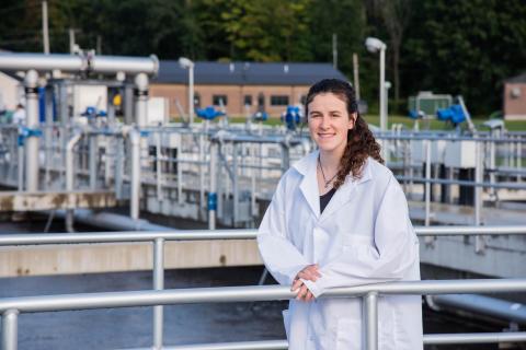 Sydney Adams stands wearing a white lab coat at a wastewater treatment facility