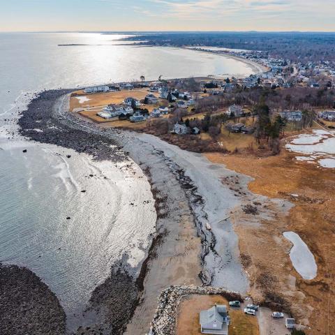 An aerial view of a rocky beach in Rye, New Hampshire where stones from the beach are washed over into a marsh on the land side of the beach.
