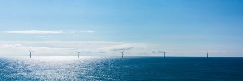 five offshore wind turbines on the horizon on a partly cloudy day, above deep blue ocean with reflecting sun