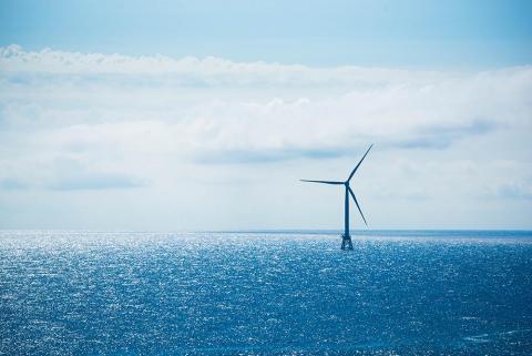 an offshore wind turbine in a blue ocean with clouds and blue sky behind it