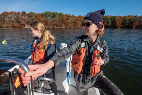 Two researchers wearing life jackets stand on a boat in great bay