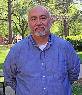 headshot of frank Lopez wearing a blue shirt in front of a forested background