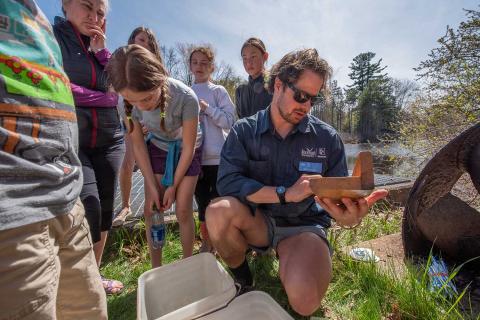 Wells Costello holds a fish measuring board in front of children learning to measure eels