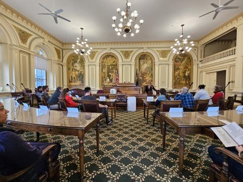 CoastWise participants sit inside at tables in the New Hampshire statehouse in Concord