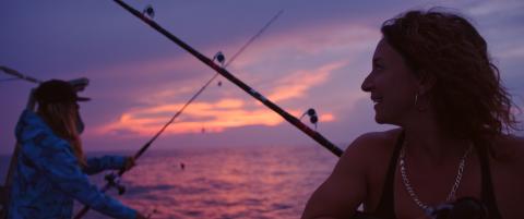 Michelle Bancewicz and Lea Pinaud gaze at their fishing rods and a fading pink sunset