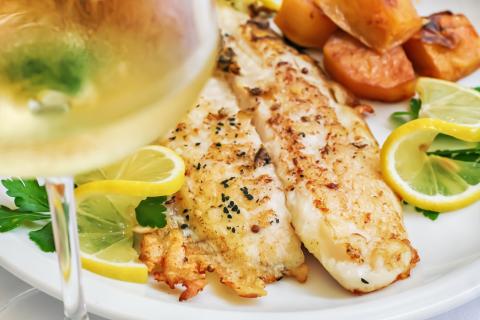 A baked white hake filet served on a plate with lemon and potatoes. 