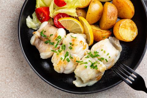 Cooked monkfish seafood on a plate with lemon, tomatoes and potatoes. 