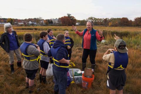 A group of students learn from a researcher about what fish species live in the salt marsh. 