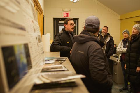 A group of Aquaculture Academy participants get a tour inside of the Coastal Marine Lab. With posters in the foreground, and staff speaking with participants in the background. 