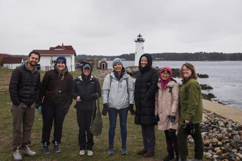 The group poses for a picture on the coast with Portsmouth Harbor Lighthouse in the background. 