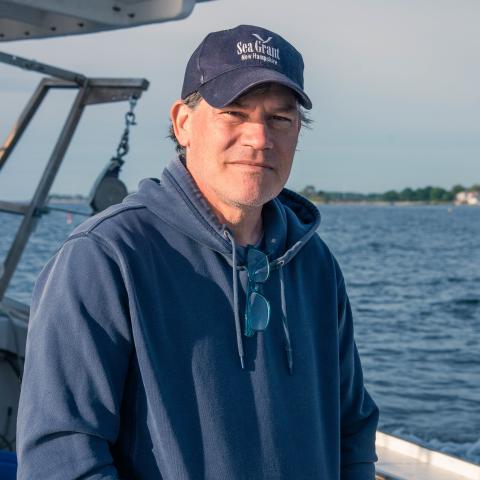A photo of Erik Chapman on a fishing vessel, with the ocean in the background.