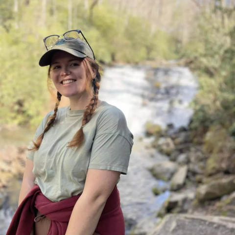 A headshot photo of Lauren George, standing in nature near a river.