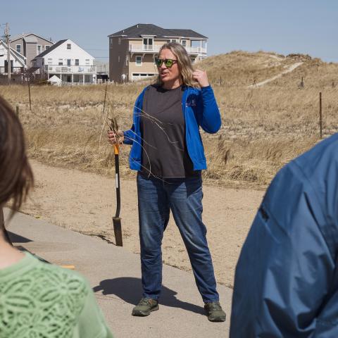 Alyson Eberhardt stands in front of a crowd, holding a shovel and beachgrass.