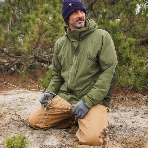 Chris Grippo kneels in the sand, with beachgrass in hand. 