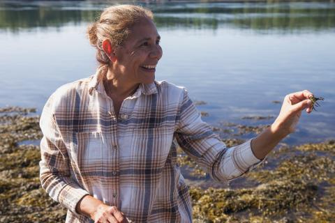 Gabriela Bradt holds up a green crab while standing in the rocky shoreline of New Hampshire. 