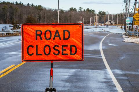 A bright orange 'road closed' sign in New Hampshire, with flooding in the background. 