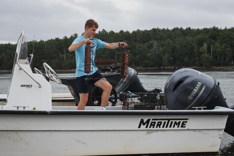 Doyle Fellow Matt walks along a docked boat with a device designed to help eelgrass grow. 