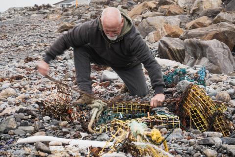 A fisherman kneels down beside a buried lobster trap, tying a metal line to the traps to help pull them out.