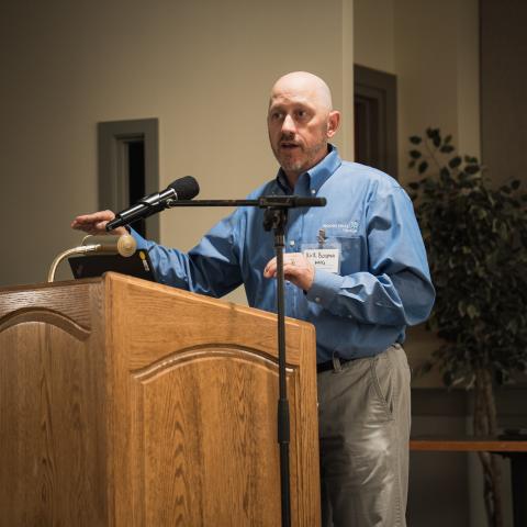 A photo of Kirk Bosma speaking at a podium.
