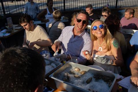 Two participants smile as they shuck oysters.