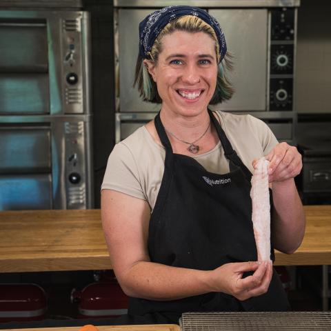 A photo of Leah Smutko in a kitchen holding up a fish for the camera.